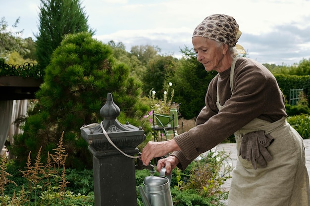 Senior woman in apron and workwear taking clean water into wateringpot