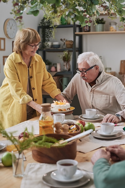 Senior woman bringing birthday cake for her husband while he sitting at dining table at home