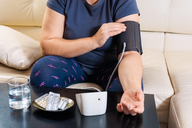 Senior woman checking blood pressure level at home older female suffering from high blood pressure sitting at a couch and using a pulsometer tonometer