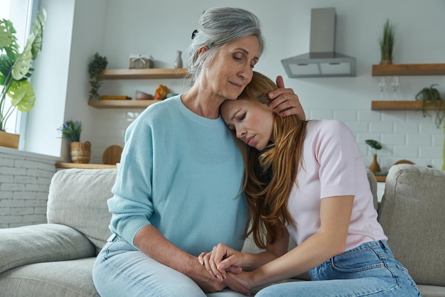 Senior woman consoling her sad daughter while sitting on the couch together