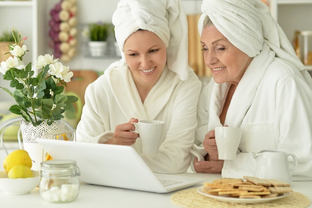 Senior woman and  daughter  in a bathrobe with laptop and tea