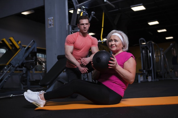 Senior woman doing situps with medicine ball working out with personal trainer