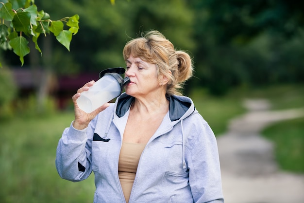 Senior woman drinks water in the park after doing sport