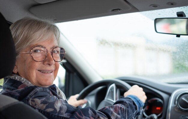 Senior woman driver driving her car on a rainy day Elderly woman holding the steering wheel looking back at camera