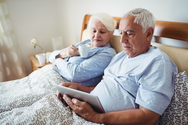 Senior woman having cup of coffee and man using digital tablet