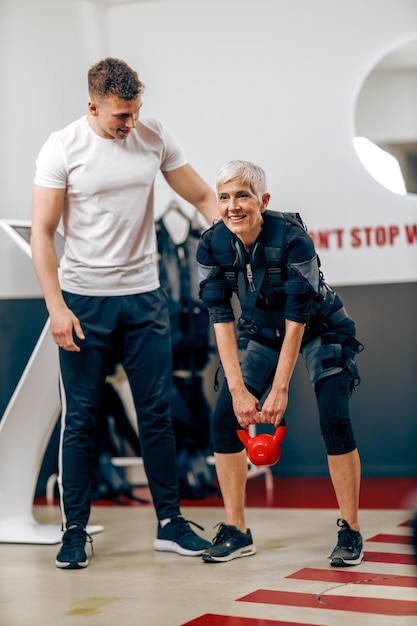 Senior woman is doing EMS training with personal trainer in the gym.