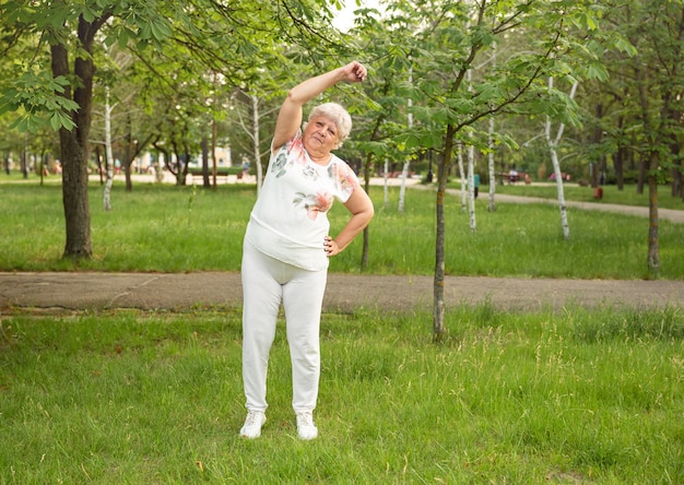 Senior woman is doing yoga and stretching exercise in the park. Smiling aged lady exercising.