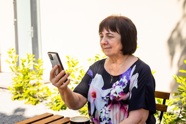 The senior woman is watching live stream at smartphone in a cafe