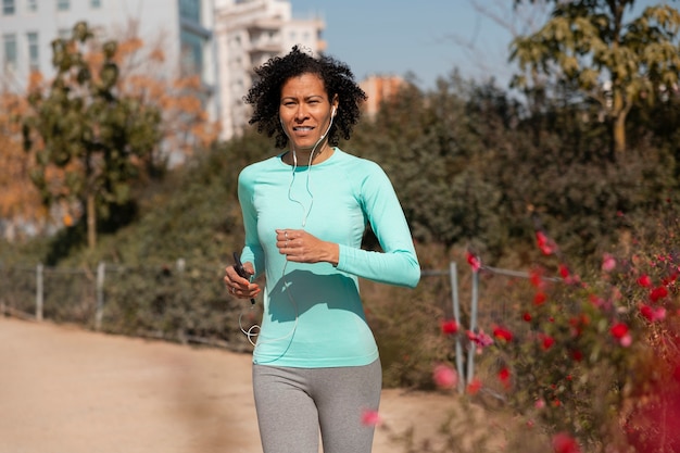 Senior woman jogging outdoors with smartphone and earphones