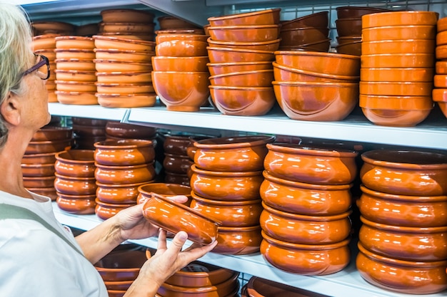 Senior woman looking and choosing a brown bowl for the table. One caucasian people. In the background a large selection of articles.  Enjoying shopping and relax