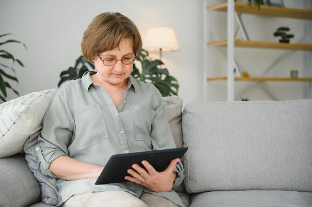 Senior woman looking and laughing at her digital tablet on sofa