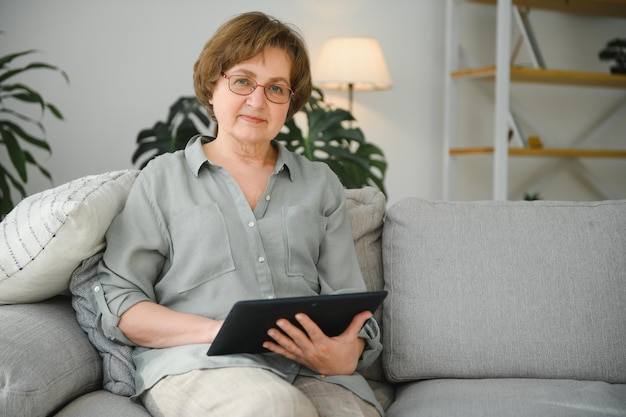 Senior woman looking and laughing at her digital tablet on sofa