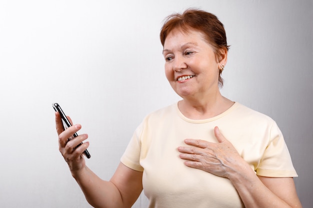 Senior woman looks at the phone on white in a light T-shirt