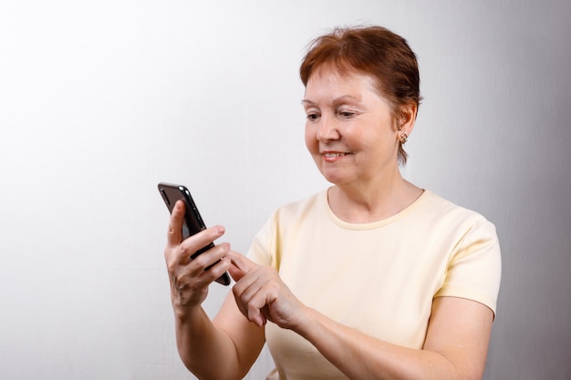 Senior woman looks at the phone on white in a light T-shirt