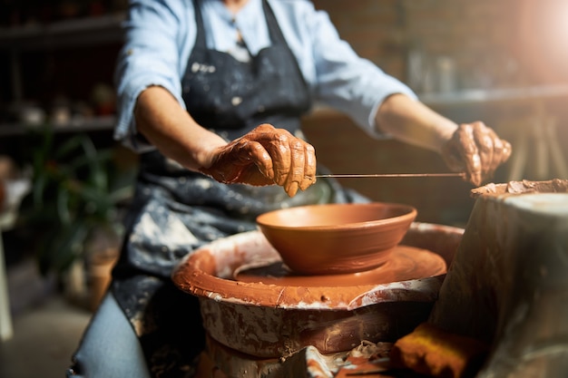 Senior woman potter using wire clay cutter while working on pottery wheel