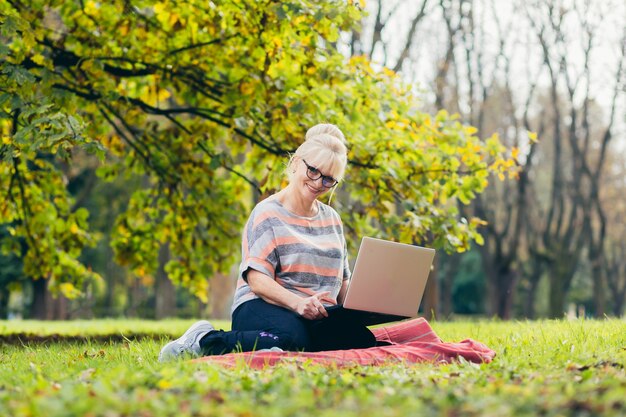 Senior woman relaxing in the park with a laptop