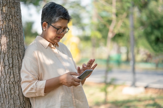 Senior woman relaxing while looking at smartphone in the park