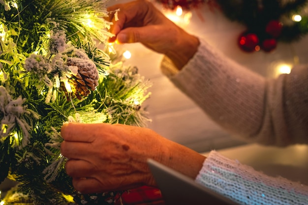 Senior woman's hands decorating a small Christmas tree with pine cones and lights