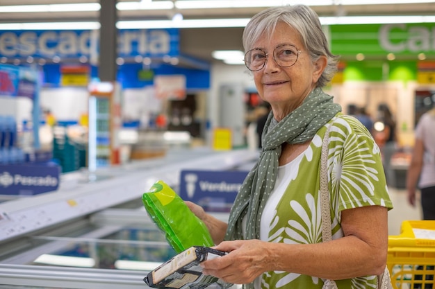 Senior woman selecting frozen vegetables in the frozen food department of the supermarket concept of consumerism price increase inflation