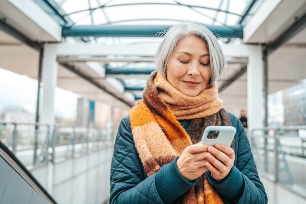 Senior woman send message with a mobile phone in a stransport station