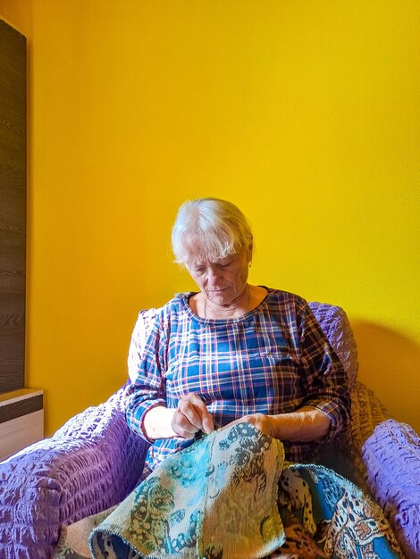 Senior woman sews wrinkled hands of the old seamstress elderly woman