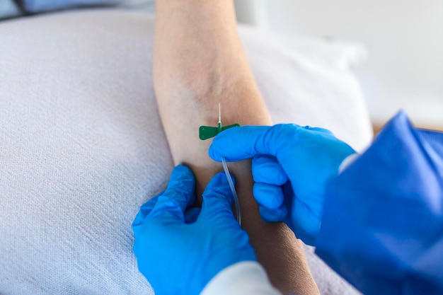 Senior woman sitting in the hospital chair while receiving IV infusion in medicine center