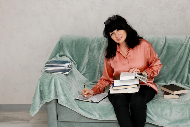 senior woman sitting on the sofa with a stack of books and taking notes