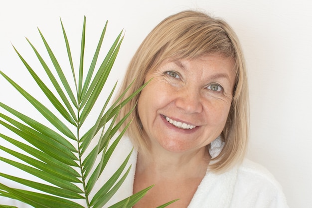 Senior woman smiling Anti-age concept with palm leaf. Mature woma face after spa treatment. Old age in joy, plastic surgery clinic, cutie grandmother, cosmetology, new senior, pensioner, mature people