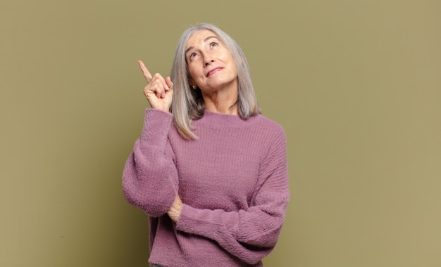 Senior woman smiling happily and looking sideways, wondering, thinking or having an idea