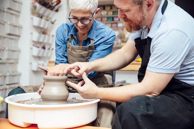 Senior woman spinning clay on a wheel with teacher at pottery class