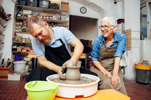 Senior woman spinning clay on a wheel with teacher at pottery class