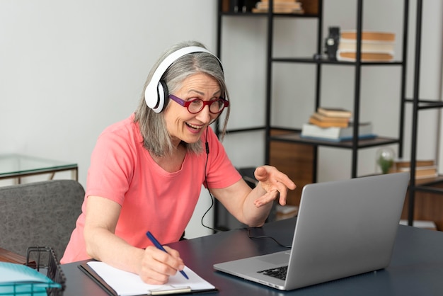 Senior woman studying at home while using laptop and taking notes