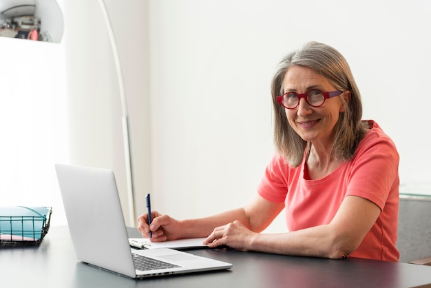 Senior woman studying at home while using laptop and taking notes