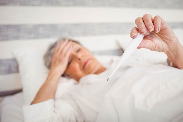 Senior woman suffer from fever checking her temperature on thermometer