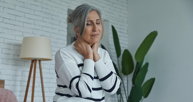 Senior woman suffering from sore throat while sitting on the bed at home