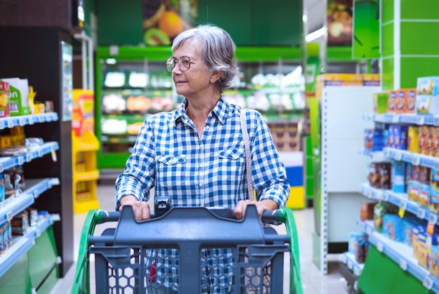 Senior woman at the supermarket pushing cart concept of consumerism inflation rising prices