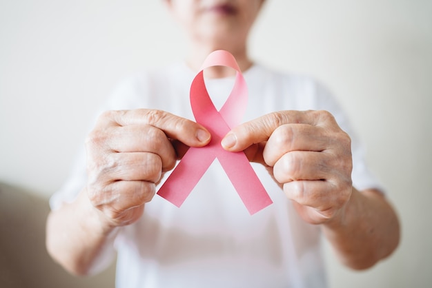 Senior woman supports breast cancer day by holding pink ribbon