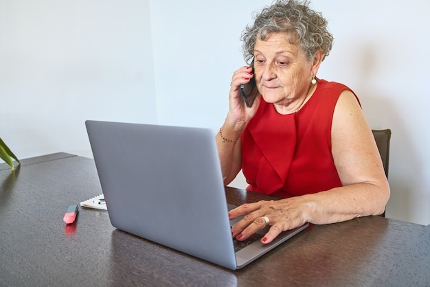 Senior woman talking on the phone while using a laptop at home