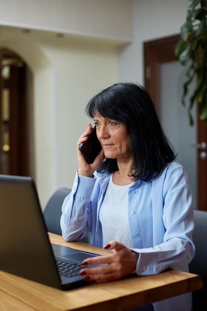 Senior woman talking speaking on phone on her workplace with laptop