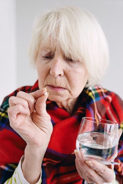 senior woman in tartan plaid with pill and glass of water Health care mature age illness concept