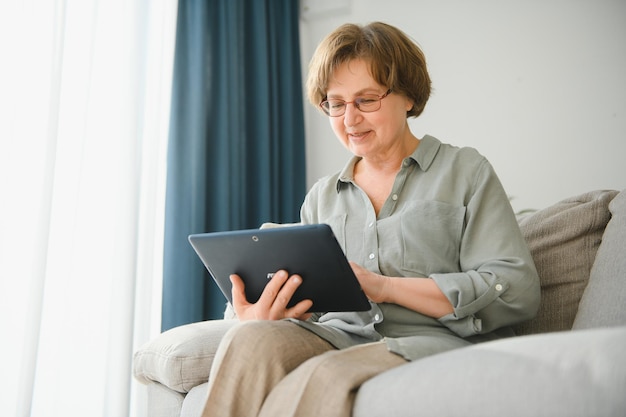 Senior woman using digital tablet in living room at home