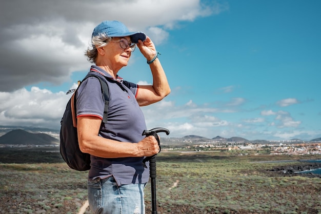 Senior woman walking on hiking day on outdoor trail on excursion between sea and countryside Relaxed caucasian woman enjoying travel adventure or retirement leading healthy lifestyle