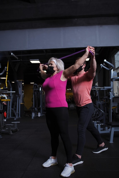 Senior woman wearing medical face mask working out at gym during coronavirus pandemic