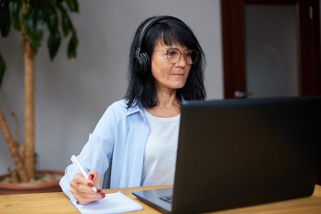 Senior woman wearing wireless headphones watch webinar, trainning