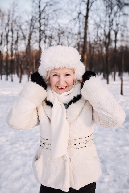 senior woman in white hat and fur coat enjoying winter in snow forest. 