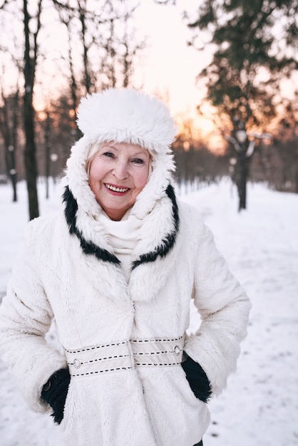 senior woman in white hat and fur coat enjoying winter in snow forest. 