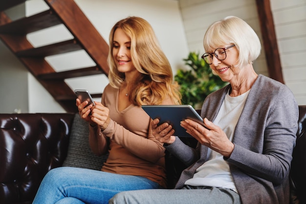 Senior women using digital tablet and middle aged woman her daughter mobile phone