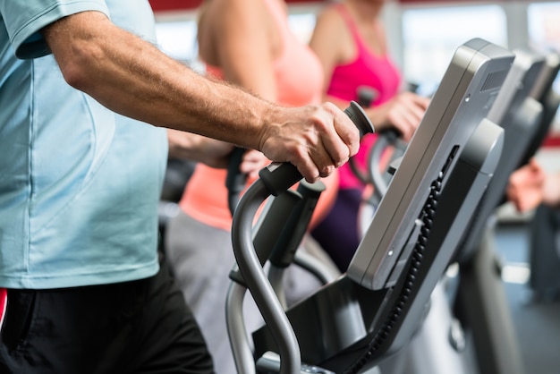 Seniors train on cross trainer with personal trainer at the gym