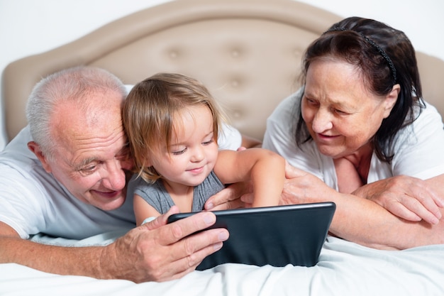 Seniors with a baby are looking at a tablet. Child with grandparents spend time together