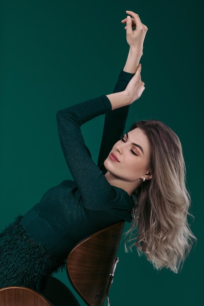 Photo sensual beautiful blonde woman in green dress sitting on chair against green background